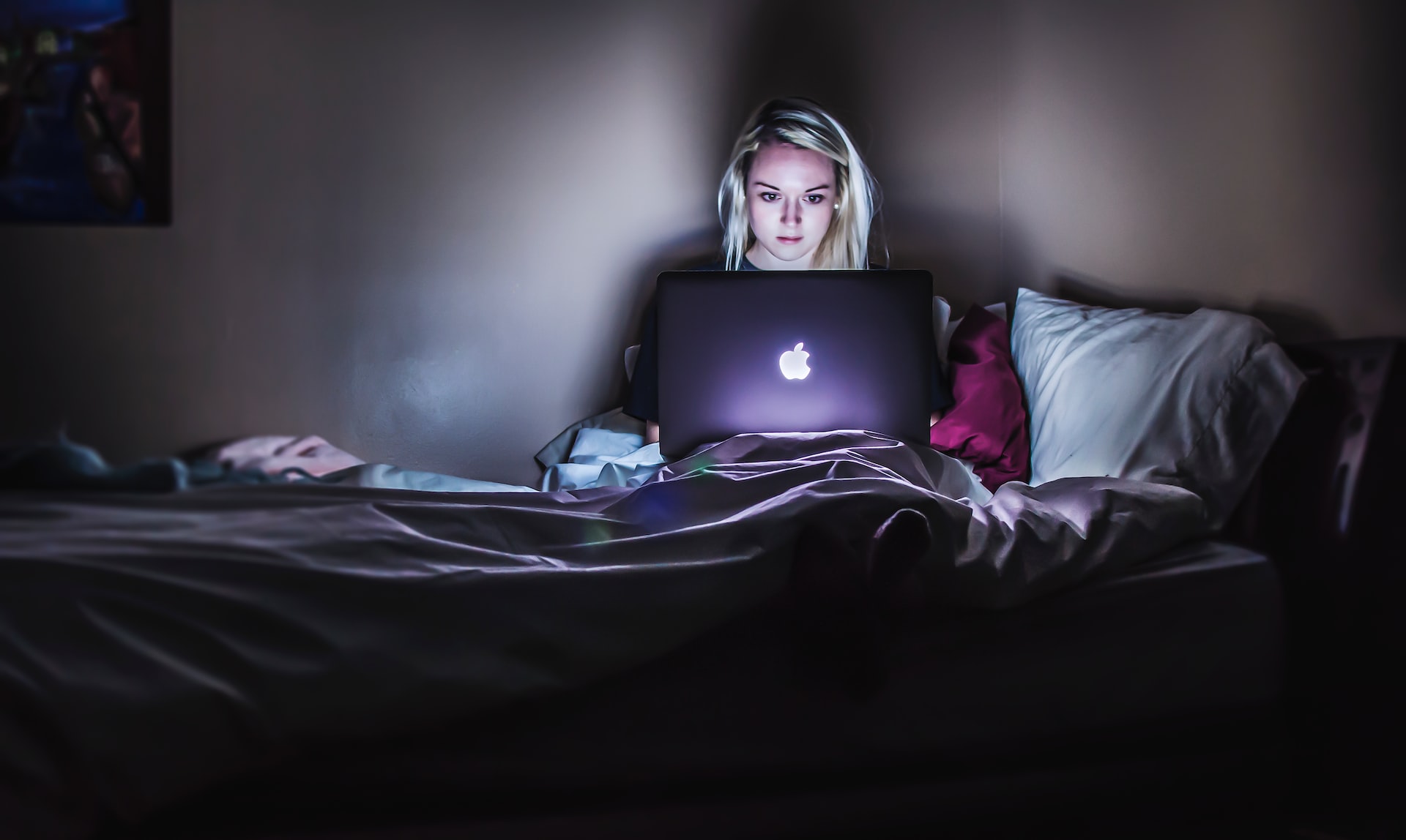 A woman on her bed, dealing with stress unhealthily by going on her laptop at night
