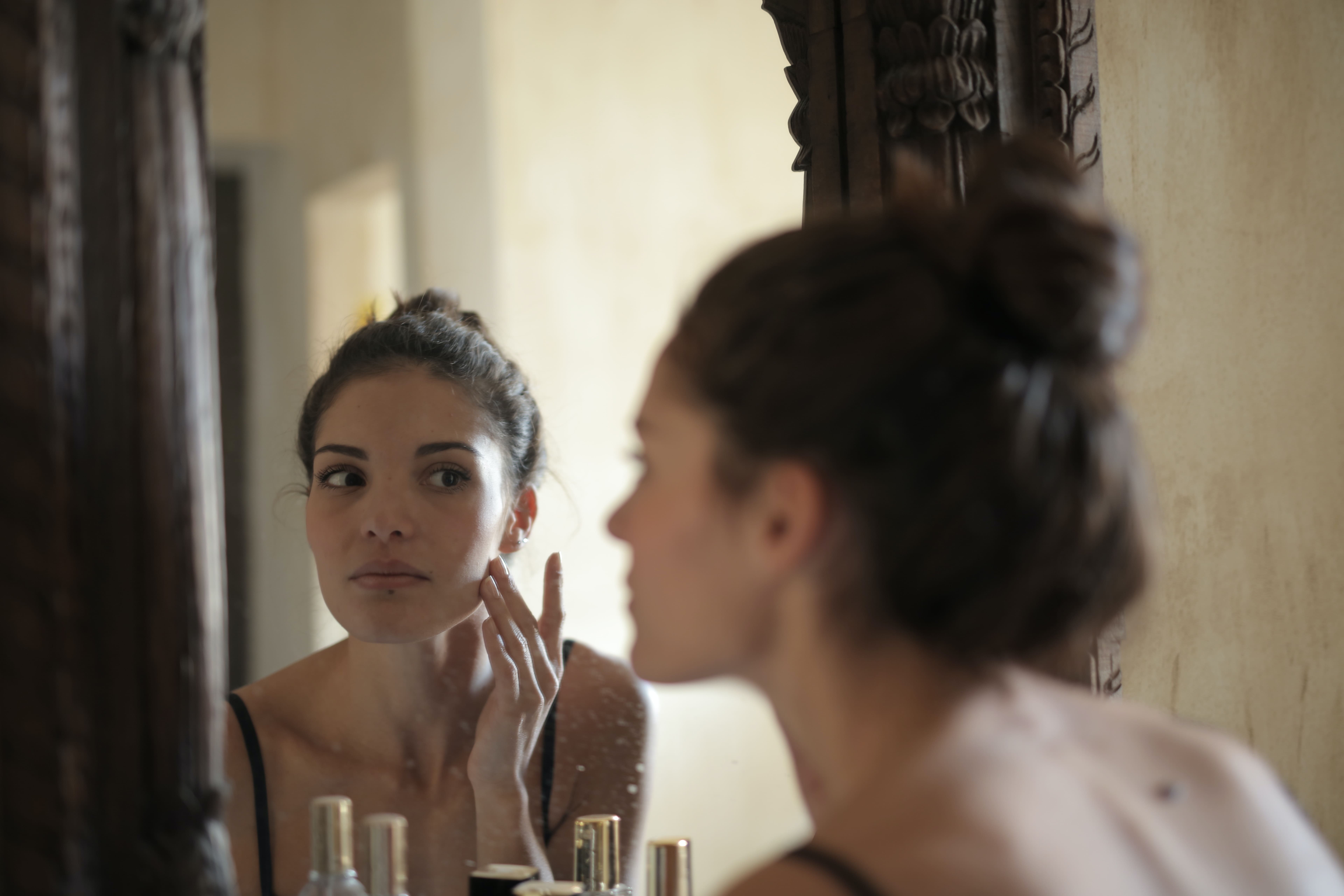A woman checking her reflection in the mirror, contemplating whether Hypobaric Oxygen Therapy could help rejuvenate her skin.