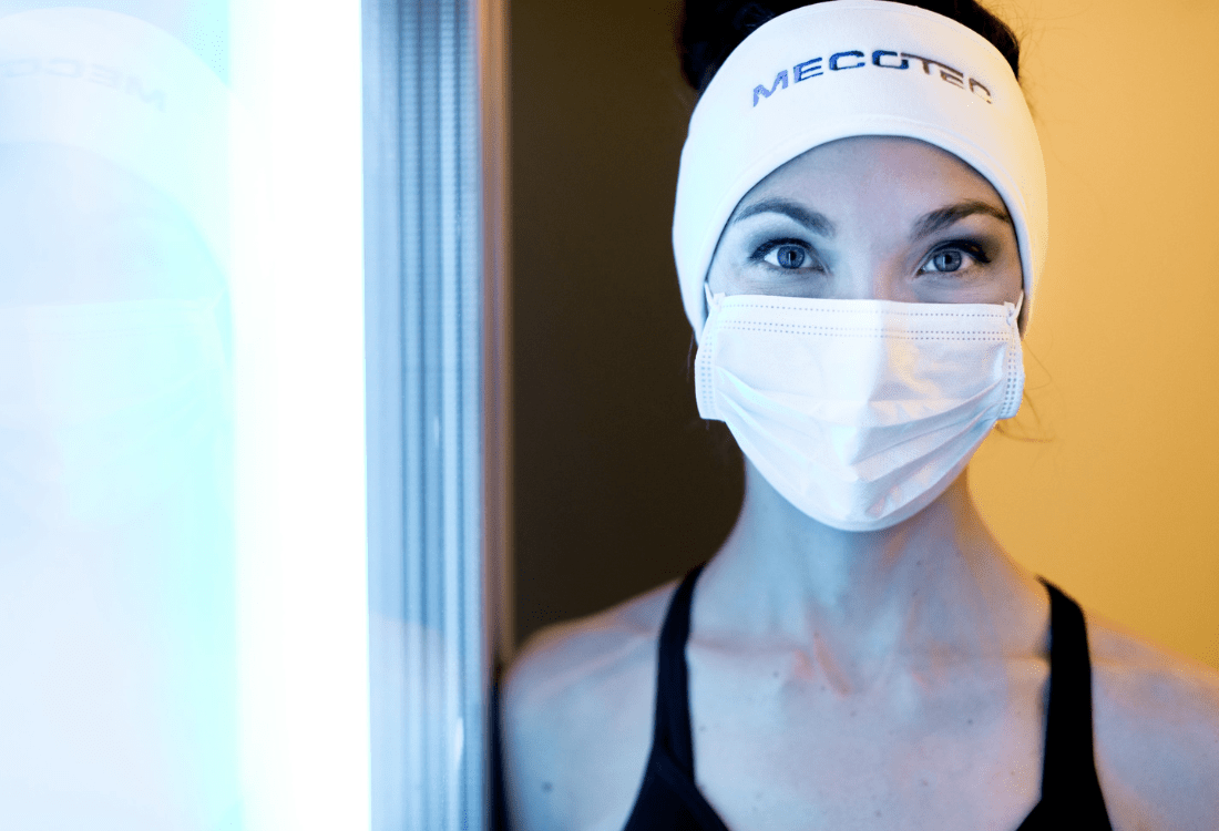 A person stands at the entrance of a cryotherapy chamber, dressed in protective headband and face mask, ready to experience the benefits of cryotherapy as part of a wellness routine.