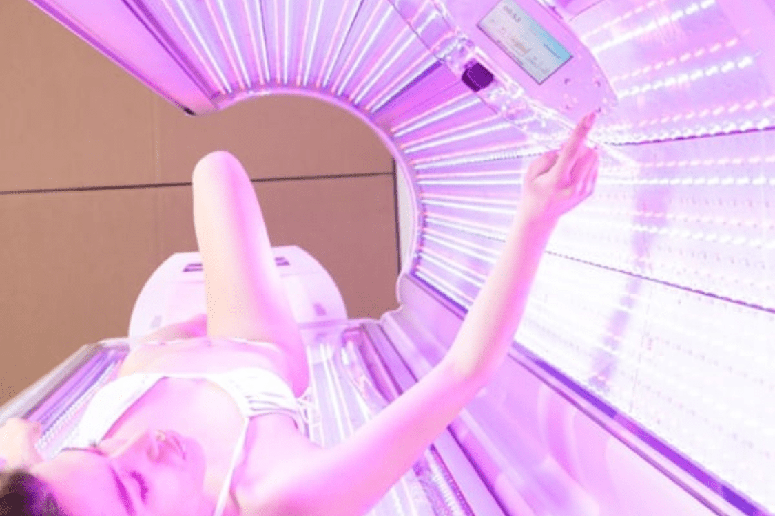 A person lies in a red light therapy bed, reaching up to adjust the settings, illustrating one of the methods to receive the therapeutic benefits of red light treatment.