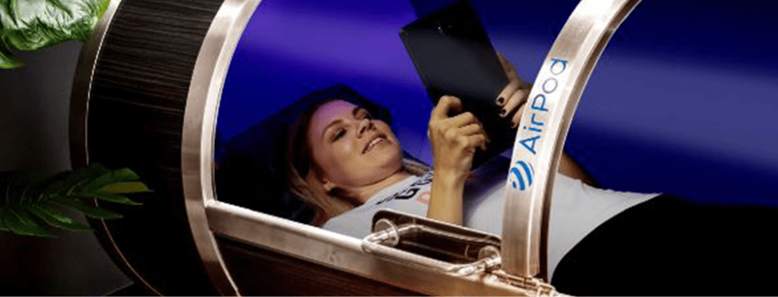 A woman lies comfortably inside a hyperbaric chamber, engaging with a tablet, researching the health benefits of molecular hydrogen as part of her wellness routine.